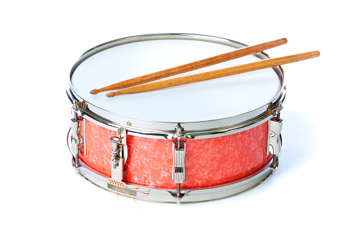 A snare red chrome tin drum with wooden drumsticks isolated on a white background.