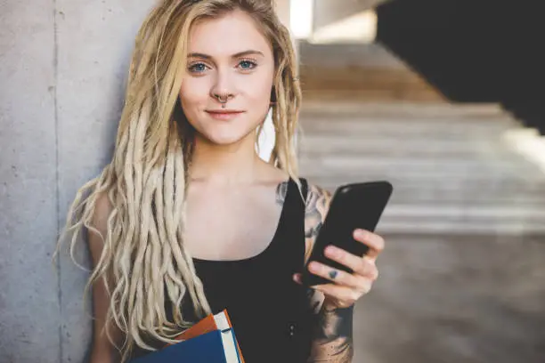 Portrait of young tattooed women with blond dreadlocks texting message on mobile phone