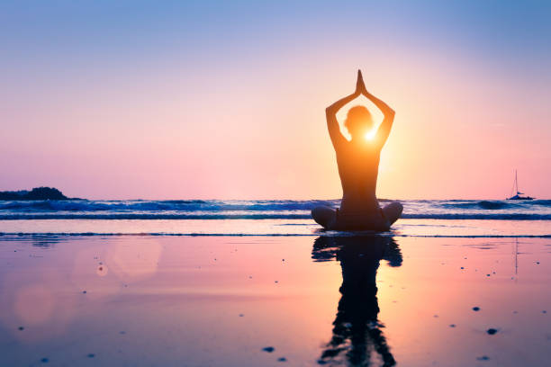 silhouette giovane donna praticando yoga posizione loto, meditando, spiaggia - beach sunset sea sunrise foto e immagini stock