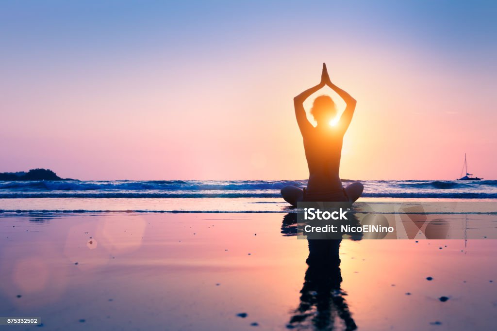 Silhouette young woman practicing yoga lotus position, meditating, beach Silhouette of young woman practicing yoga, lotus position, and meditating on the beach Yoga Stock Photo