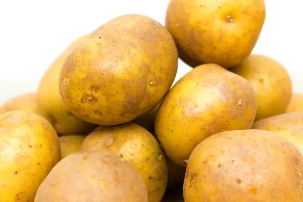 Piled up yellow orange potatoes against a white background