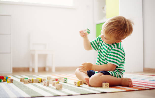 木製キューブで床に座っている 2 歳児 - アルファベットの写真 ストックフォトと画像