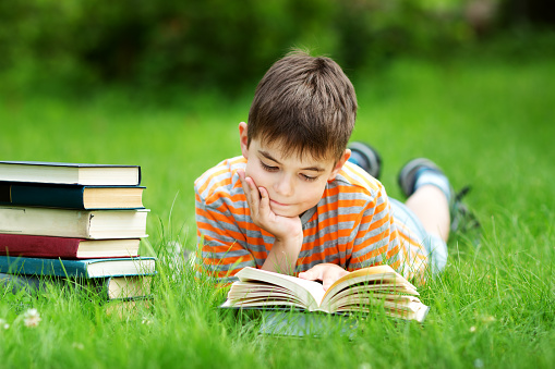 seven years old child reading a book lying on the grass