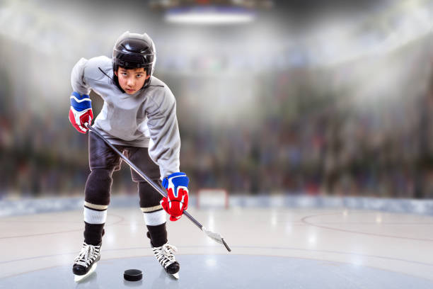 Low angle view of hockey player handling puck on ice with sports arena full of fans in the stands and copy space. Shallow depth of field on background. Fictitious background arena created in Photoshop.