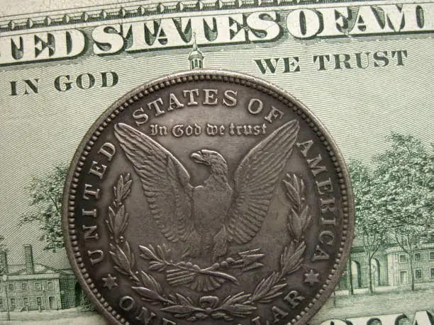 In God we trust – US nation’s motto on banknote and Morgan dollar coin. Antique and modern money to make profit and income. Closeup macro symbol of economy, finance and investment. Bill of hundred and one dollar coin minted by Federal reserve