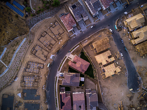 Top down aerial shot of suburban tract housing under construction near Santa Clarita, California. The houses vary in completion from a bare foundation to half tiled roofs.