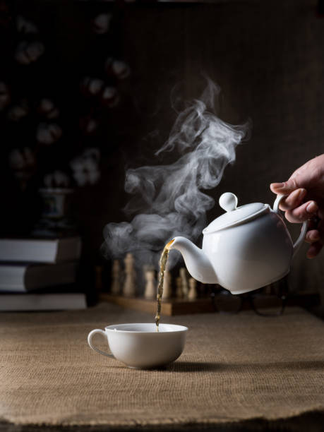 pouring black hot tea into cup on the background of the interior - кувшин imagens e fotografias de stock
