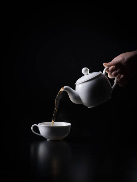 pouring black hot tea into cup on the black background. - кувшин imagens e fotografias de stock