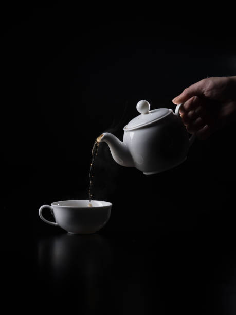 pouring black hot tea into cup on the black background. - кувшин imagens e fotografias de stock