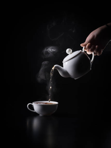 pouring black hot tea into cup on the black background. - кувшин imagens e fotografias de stock