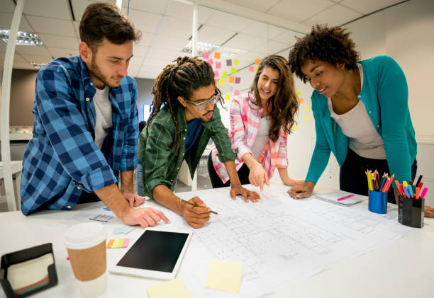 istock Multi ethnic group of designers at the office working on a blueprint pointing and smiling 875430178