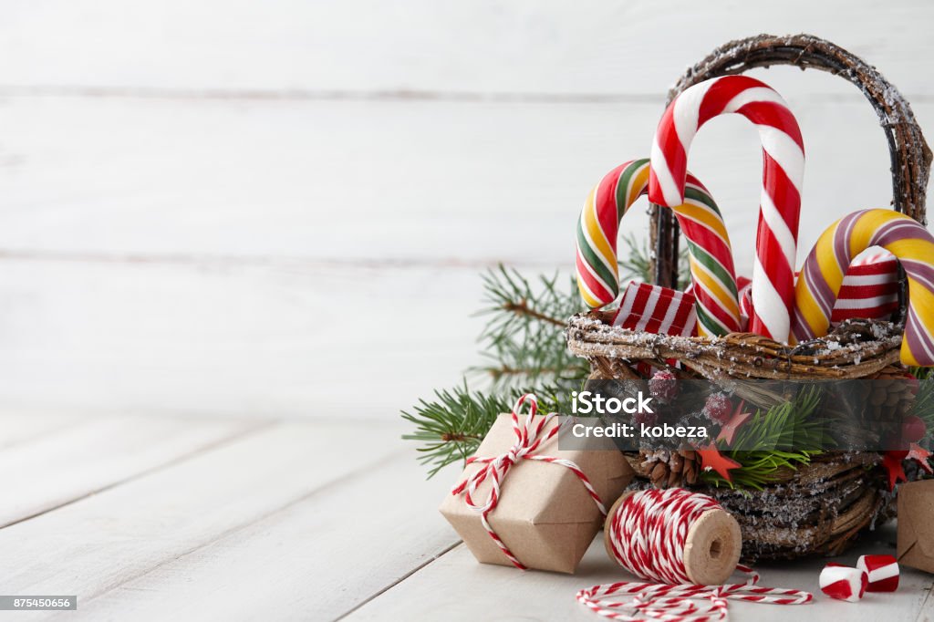 Christmas basket with candy canes on white planks Christmas wicker basket with striped candy canes and gifts on white wooden table, festive decoration Basket Stock Photo