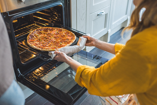 Cropped shot of young woman  taking pizza from oven