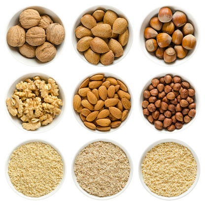 Walnuts, almonds and hazelnuts in white bowls. Whole, shelled and grounded nuts. Prunus dulcis, Corylus avellana, Juglans regia.  Macro food photo, close up, from above, isolated, on white background.