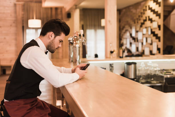 istock Waiter sitting at bar counter with smartphone 875478450