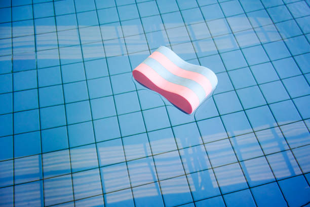 Pink and blue Pull buoy floating abandoned in swimming pool lonely against square tile floor and building silhouette. stock photo