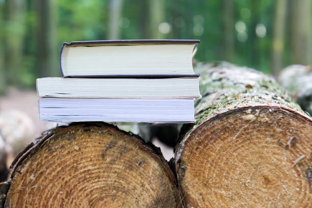istock Three books lying on felled trees,  Save the trees - read e-books 875540434