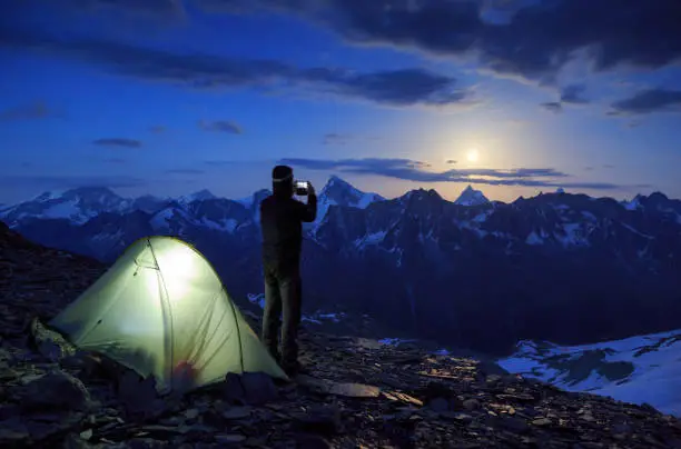Mountaineer taking a photo with his smartphone of the moon rising above the famous Matterhorn mountain, Switzerland.
