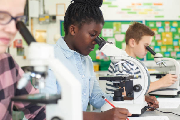 gruppo di alunni che usano i microscopi in classe di scienze - educazione secondaria di scuola media foto e immagini stock