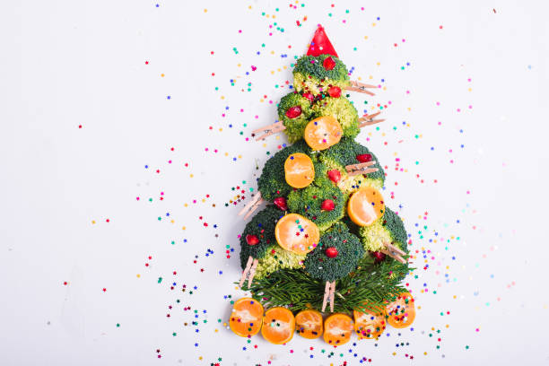 Christmas tree made of vegetables Christmas tree made of broccoli, mandarins, pomegranate seeds with glitter isolated on white background. Holiday decorations and meals. pomegranate in spanish stock pictures, royalty-free photos & images