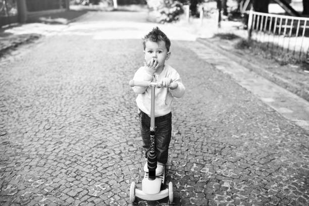 Cute little boy riding scooter outdoor on the street, black and white