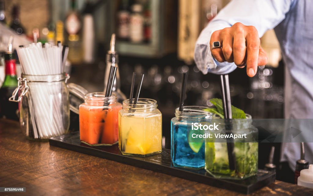Bartender hand at multicolored fashion drink with straw on vintage glass cups in fashion cocktail bar - Food and beverage concept with professional barman working at mixology restaurant - Vivid colors Drink Stock Photo