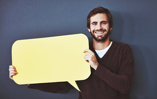 Studio portrait of a young man holding a speech bubble against a grey background