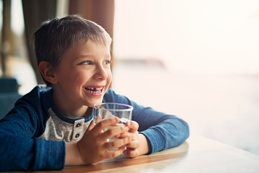 Portrait of a little boy aged 7 drinking a glass of water.
