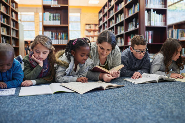 The library is their favourite place to learn Shot of a group of elementary school kids and their teacher lying down while working in the library elementary student with teacher stock pictures, royalty-free photos & images