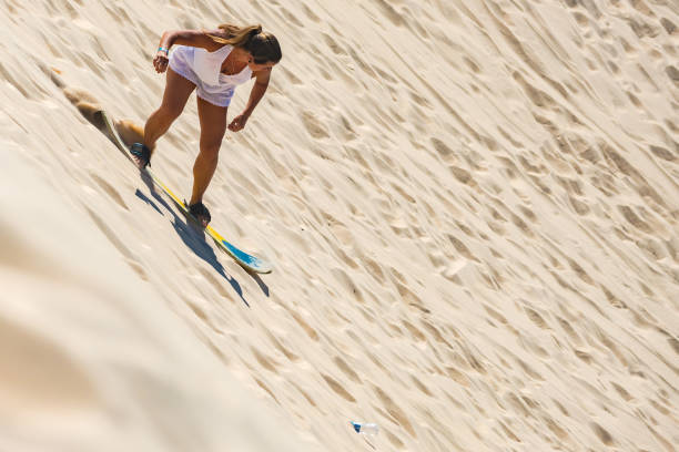 Anna Bay, Australia - January 15, 2014: A woman sandboards down a large sand dune before other tourists at Stockton Beach.