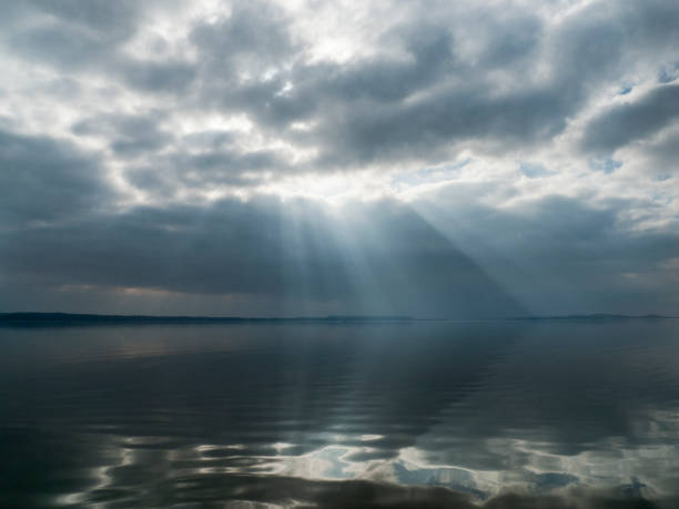 Stormy clouds in a low key image of a lake with sunbeams breaking through. Nature landscape on the sea, wonders  of our planet.