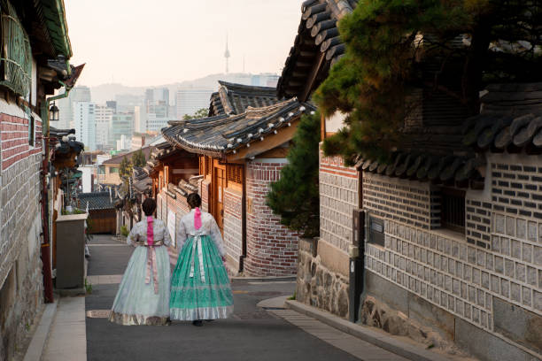 Back of two women wearing hanbok walking through the traditional style houses of Bukchon Hanok Village in Seoul, South Korea. stock photo