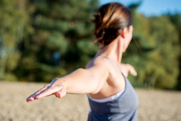 Young blonde woman doing yoga on the beach. Wearing leggings with a blue tshirt, doing first warrior pose.