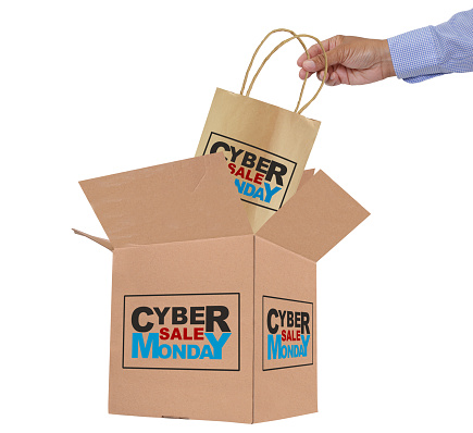 Hand placing Cyber Monday Sale shopping bag  into open cardboard box white background