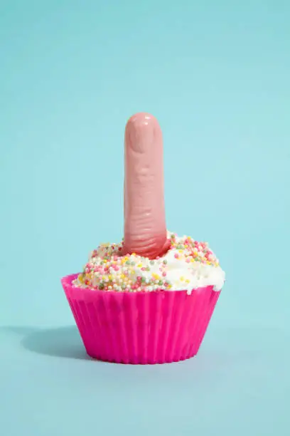 a simple pink silicone cupcake mold filled with whipped cream and sprinkles on it and a plastic finger inside on a vibrant turquoise blue pop background. contrast colors. Minimal quirky still life photography.