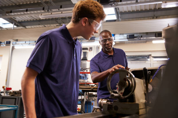 istock Engineer Showing Teenage Apprentice How To Use Lathe 875674216