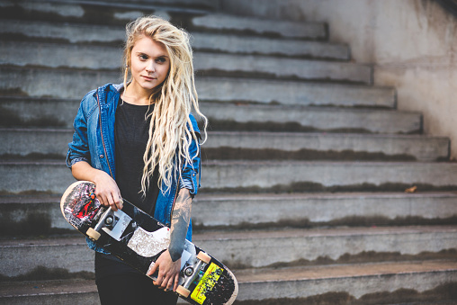Portrait of young tattooed woman with blond dreadlocks against staircase