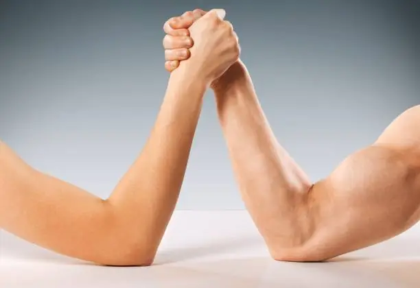 Cropped photo of Man and woman doing arm wrestling over grey background