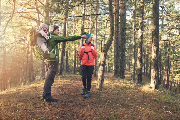 young family on forest hike on sunny autumn day - mother holding child pointing imagens e fotografias de stock