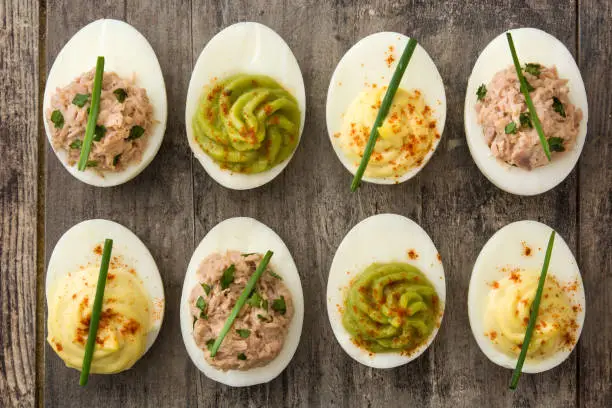 Variety of stuffed eggs with tuna and guacamole on wooden background