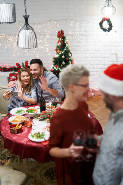 istock Cute young couple waving and taking a selfie while sitting at the table on Christmas lunch with friends. 875700242