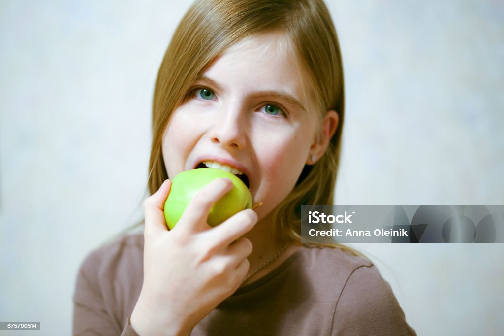 Beautiful young girl eating green Apple Beautiful young girl eating green Apple, light background Adult Stock Photo