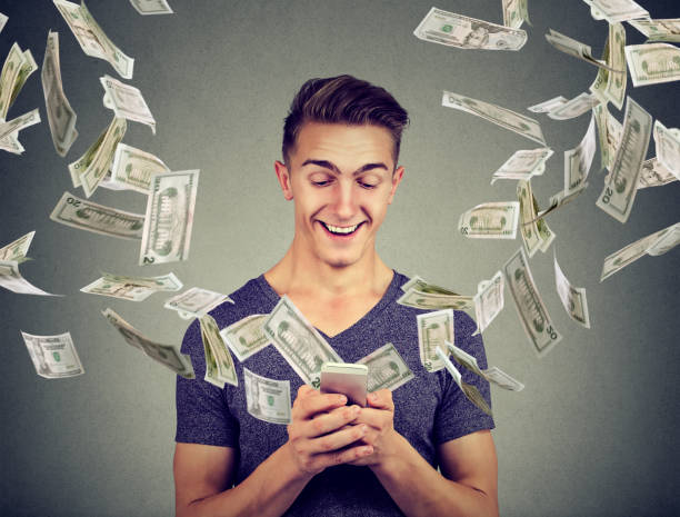 istock Online banking money transfer, e-commerce concept. Young man using smartphone with dollar bills flying away from screen 875753258