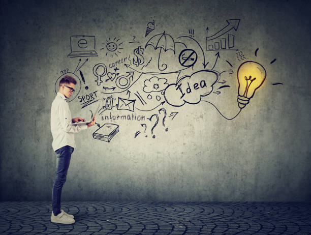 istock Young man using a laptop with light bulb plugged in it and info graphic plan written on concrete wall 875753422