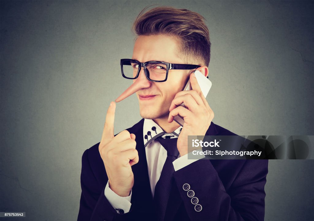 young sly man with long nose talking on mobile phone isolated on gray wall background. Liar concept. Human emotion feelings Dishonesty Stock Photo