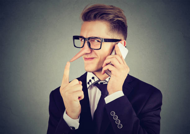 young sly man with long nose talking on mobile phone isolated on gray wall background. Liar concept. Human emotion feelings young sly man with long nose talking on mobile phone isolated on gray wall background. Liar concept. Human emotion feelings falsehood stock pictures, royalty-free photos & images