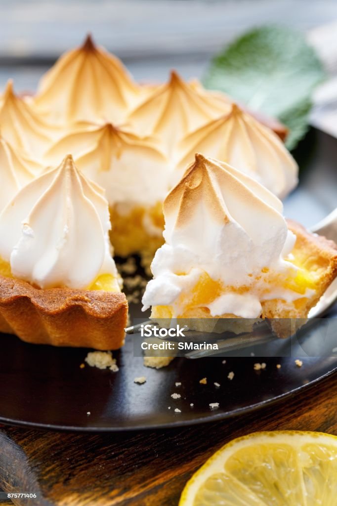 Piece of lemon tart on a fork closeup. Plate of lemon tart and meringue on wooden table, selective focus. Meringue Stock Photo