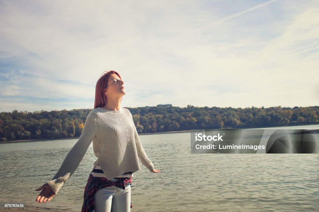 Enjoying in sunshine by the river. Woman with arms wide open enjoying in sunshine by the river. Enjoying life and breathing fresh air with eyes closed. Holding Breath Stock Photo