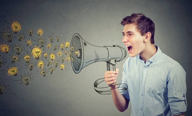 istock Man screaming out his ideas loud in megaphone isolated on gray wall background 875810376