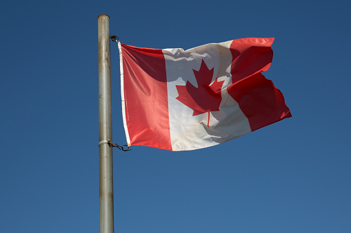 Canadian flag waving in the air over a beautiful blue sky